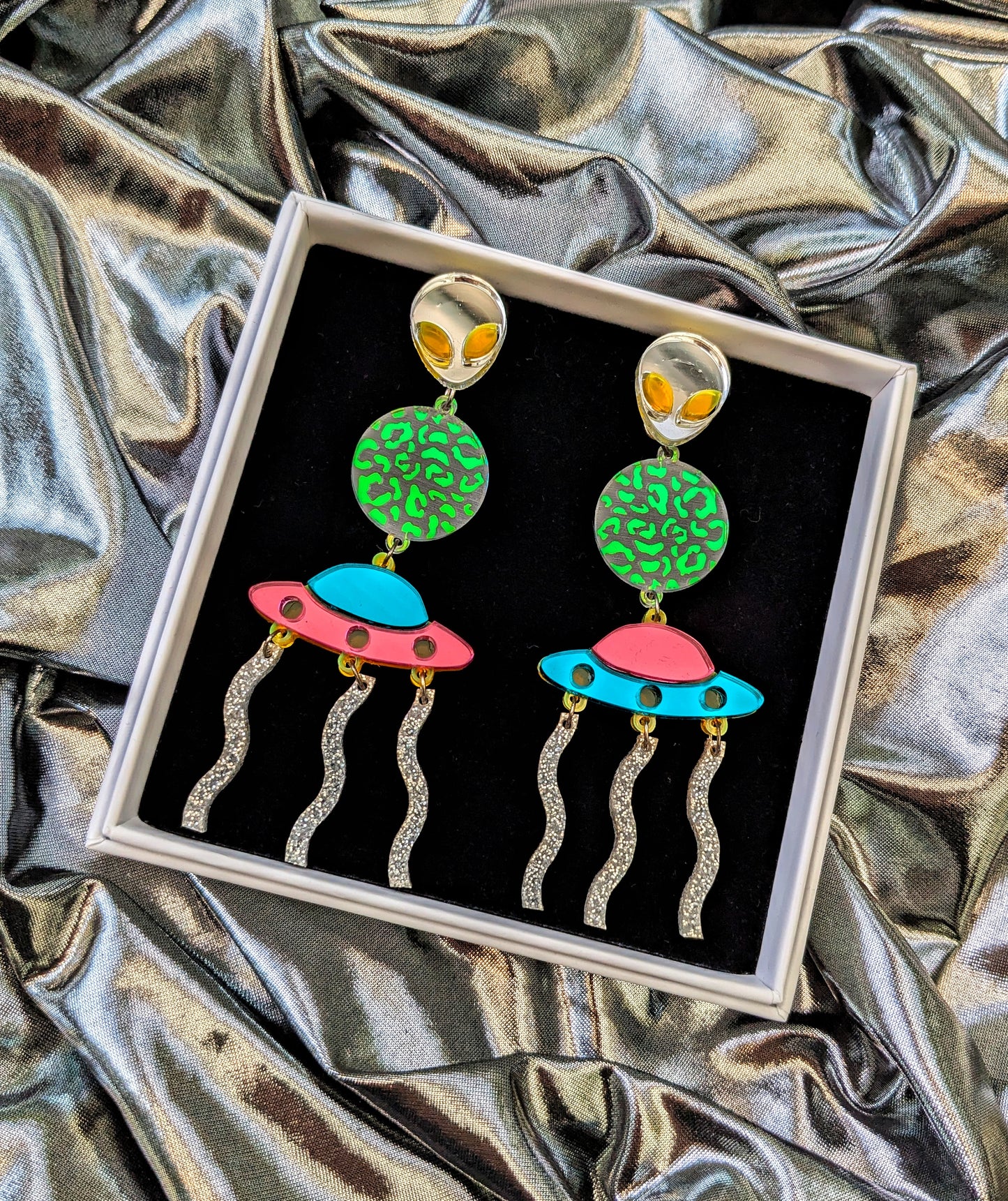  Silver Lasers Statement Earrings with silver and neon green acrylic Alien, a transparent planet with iridescent mermaid acrylic leopard print detailing, Mismatching Pink and Turquoise Mirrored Acrylic Spaceship, and silver sparkly acrylic laser beams