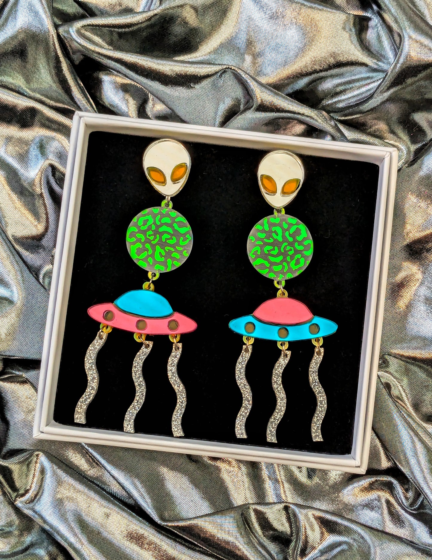  Silver Lasers Statement Earrings with silver and neon green acrylic Alien, a transparent planet with iridescent mermaid acrylic leopard print detailing, Mismatching Pink and Turquoise Mirrored Acrylic Spaceship, and silver sparkly acrylic laser beams