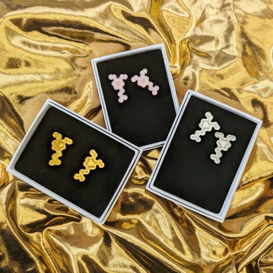 Display of dopamine molecule stud earriings in gold, pink and silver boxed on a gold fabric background