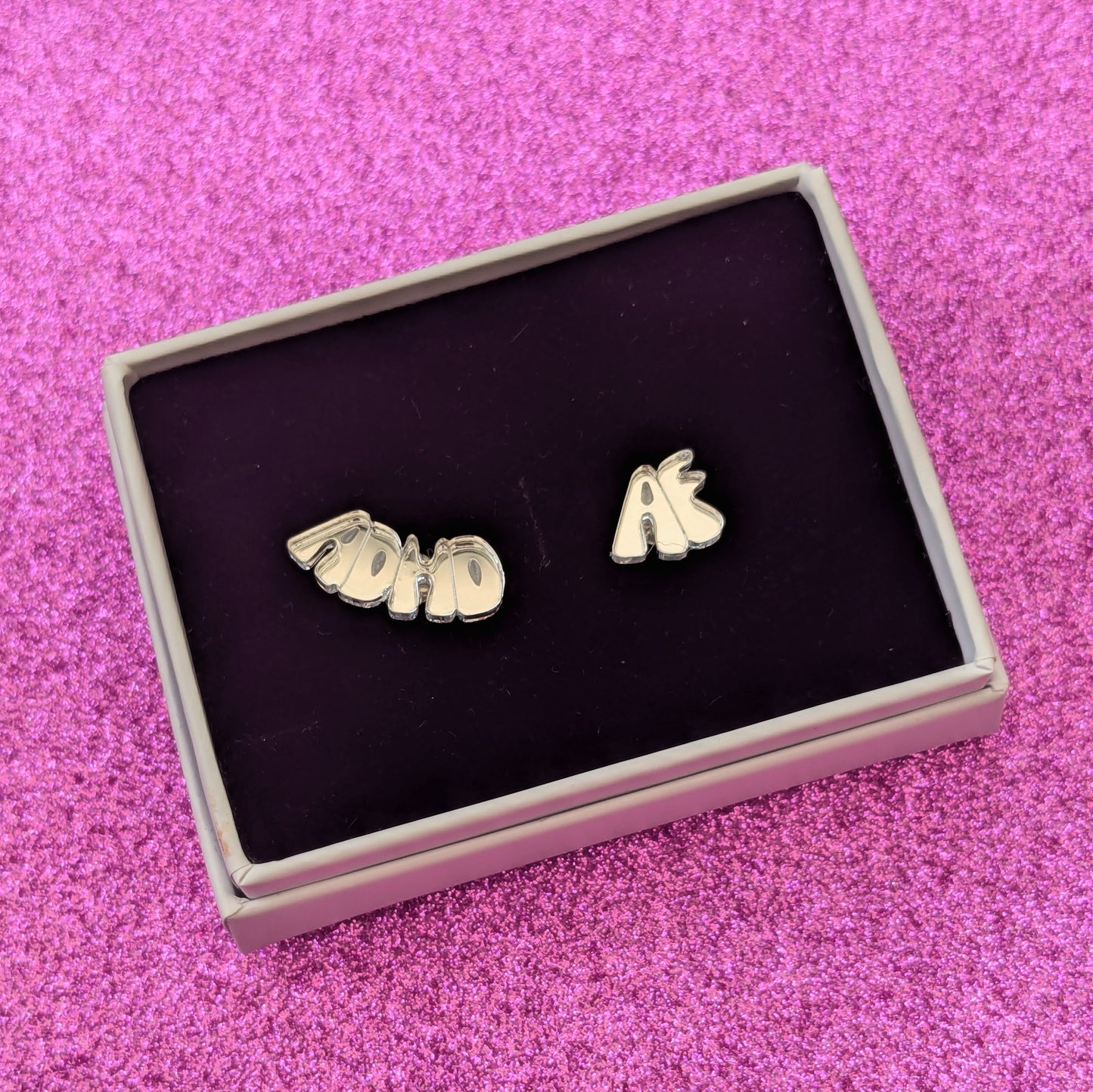 Small Silver ADHD AF stud earrings boxed on a pink glittery background