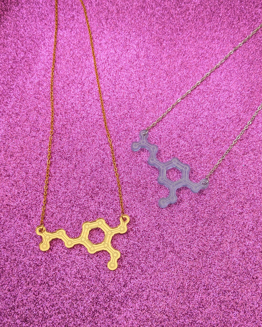 Two acrylic necklaces on in blue one in gold with the dopamine molecule design on