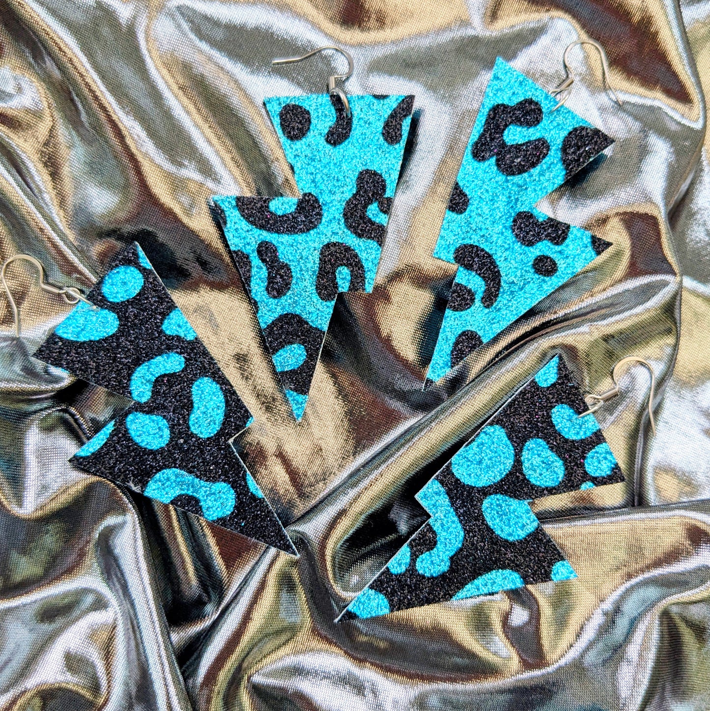 Medium leopard print lightning bolt earrings in turquoise and black glitter fabric