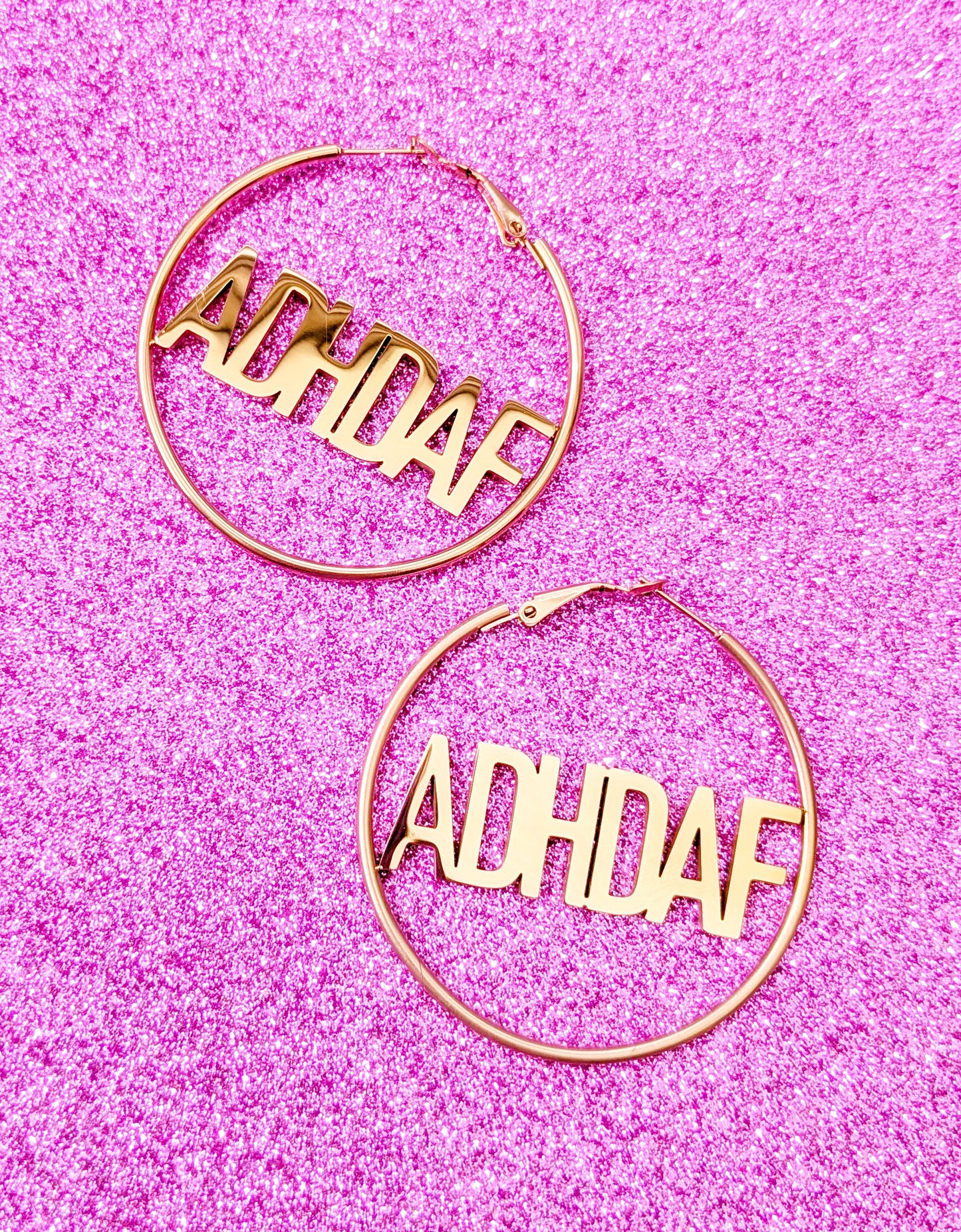 Rose Gold Hoop Earrings with letters ADHDAF across middle on a pink glittery background