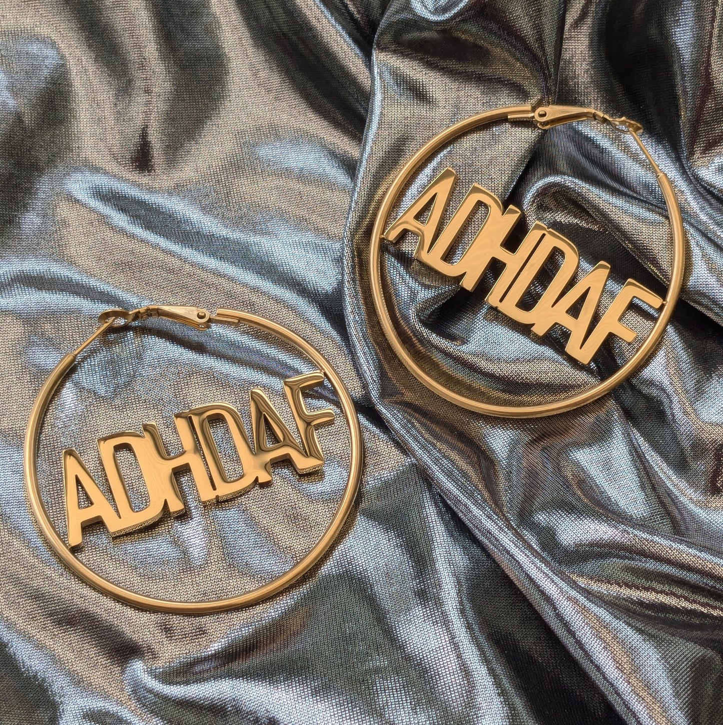 Rose Gold Hoop Earrings with letters ADHDAF across middle on a silver fabric background