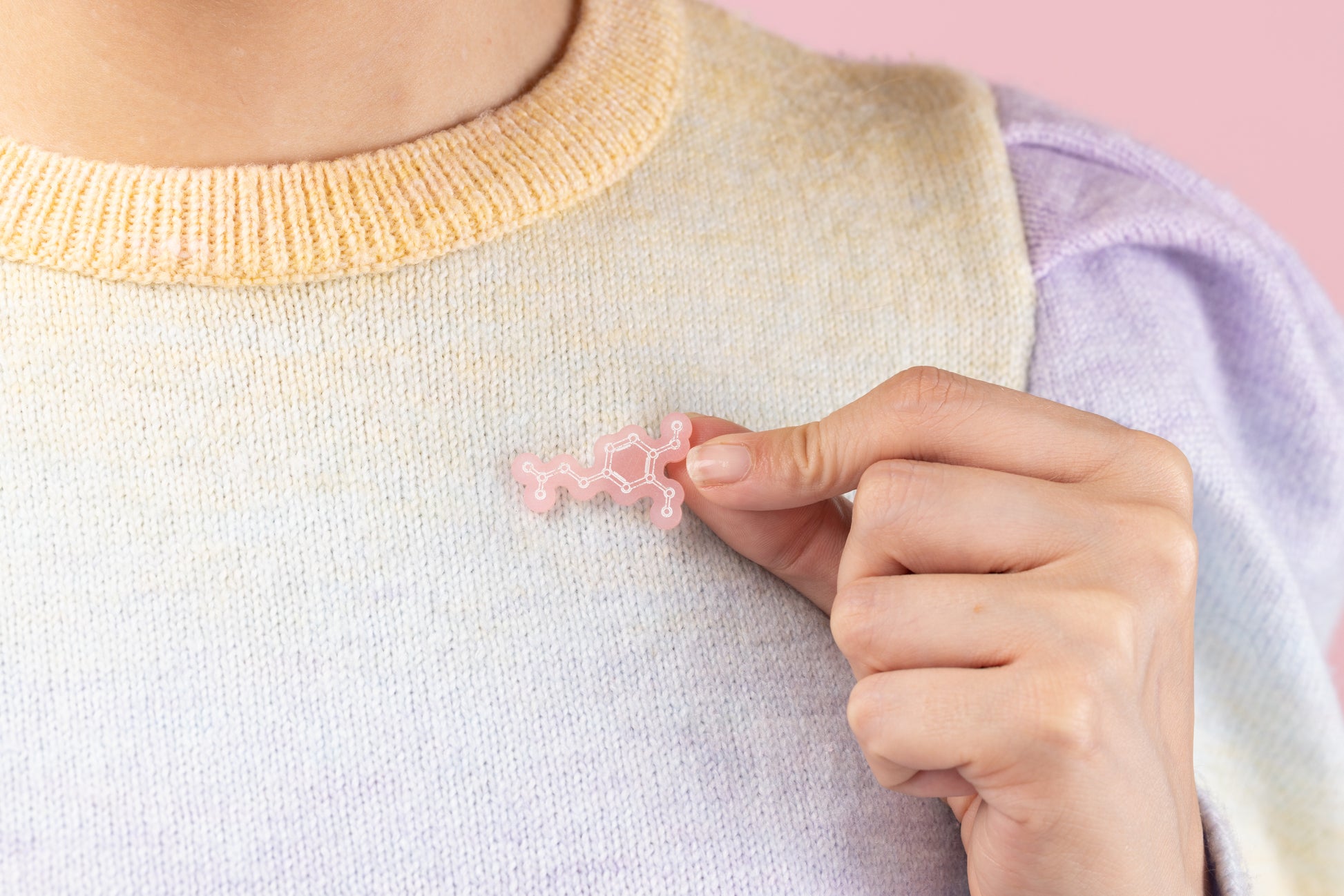 Model holds pink dopamine molecule pin next to her jumper