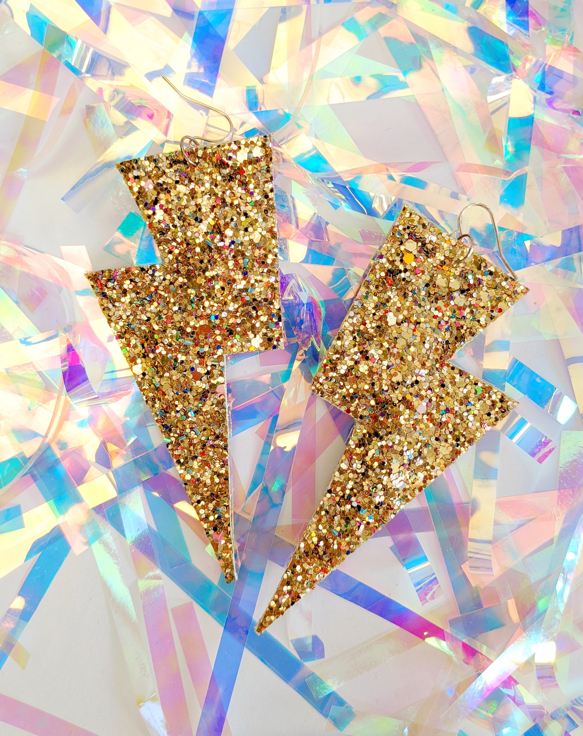 Large gold glittery lightning bolt earrings on a tinsel background