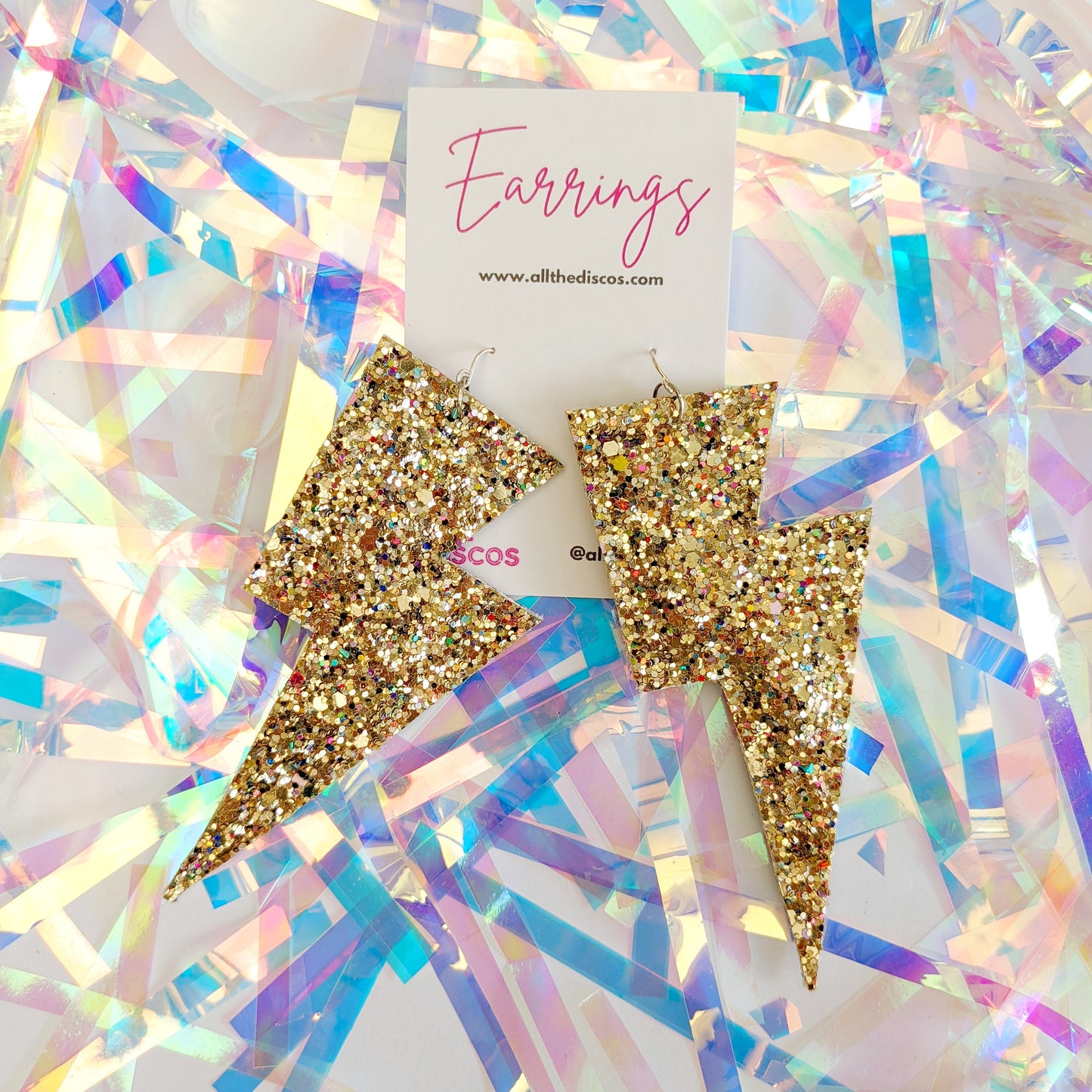 Large gold glittery lightning bolt earrings on a tinsel background