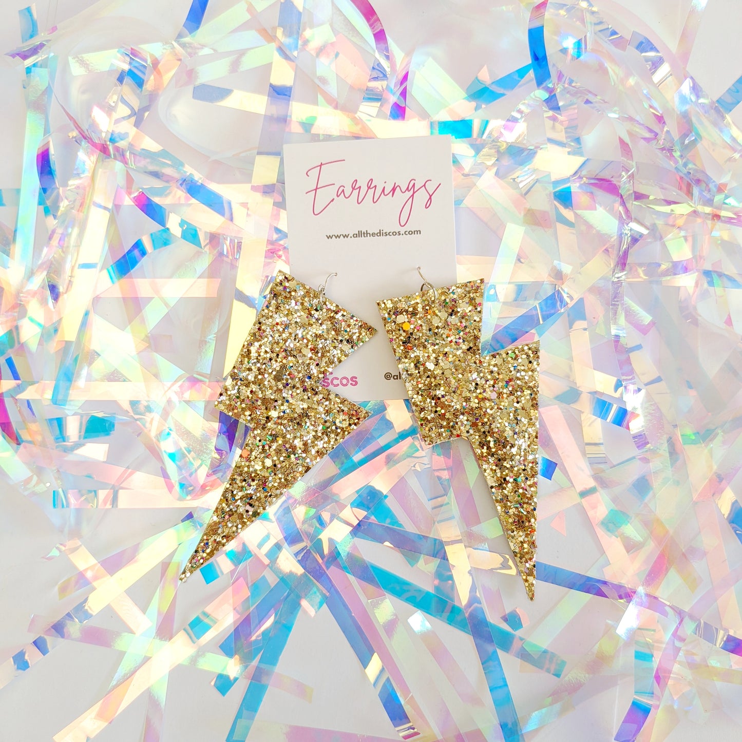 Large gold glittery lightning bolt earrings on a tinsel background