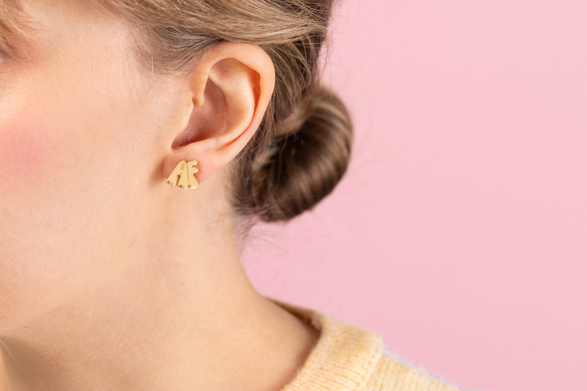 Model wearing small gold acrylic stud earring with the letters AF on them