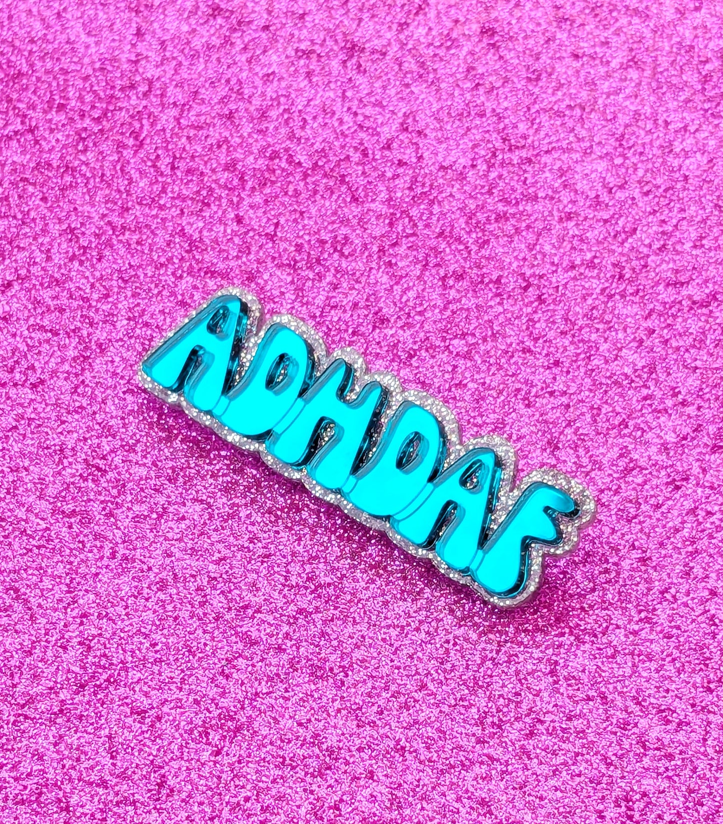 Turquoise acrylic ADHDAF pin on a glittery pink background