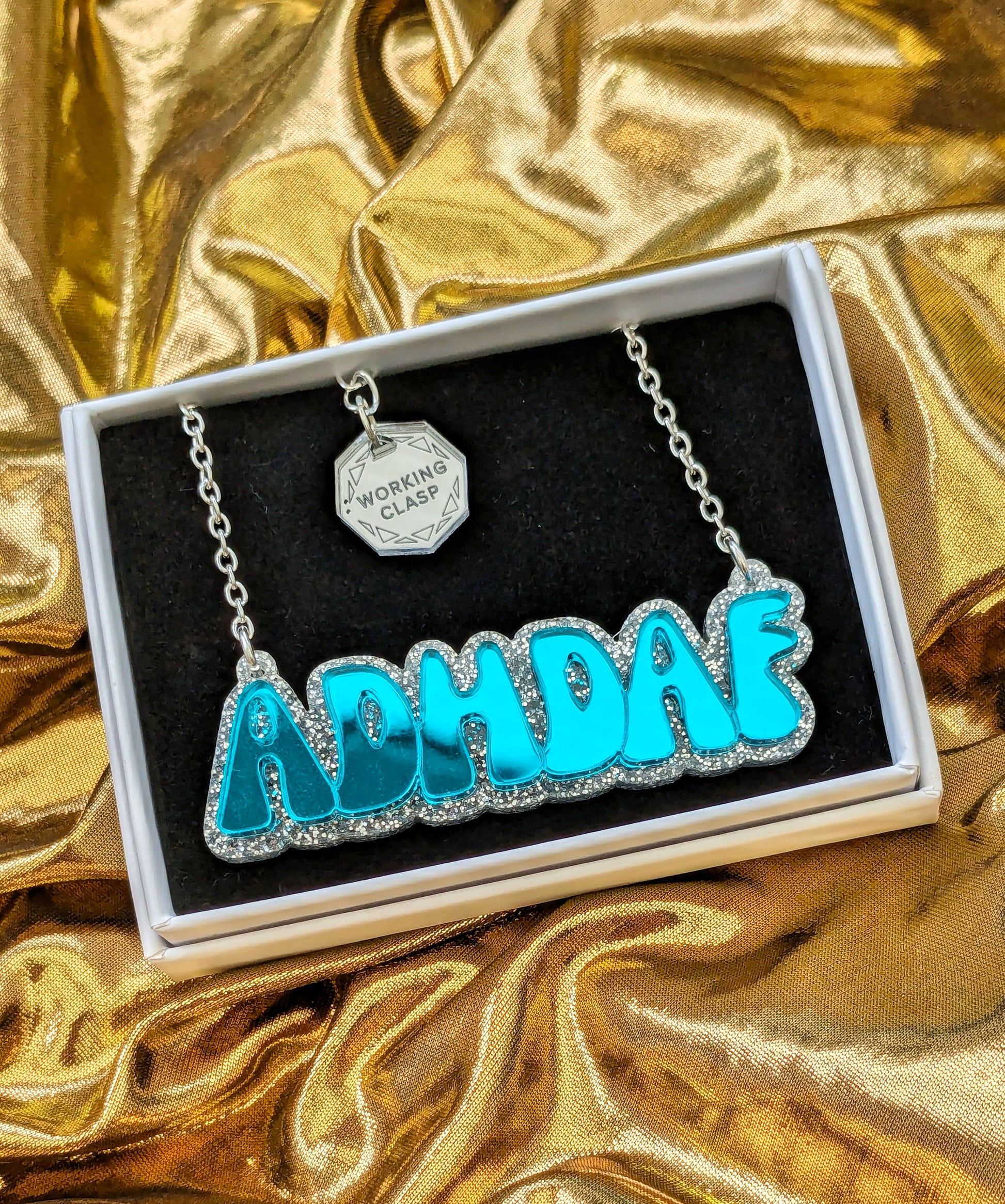 ADHDAF acrylic necklace in turquoise on silver chain boxed on a gold fabric background