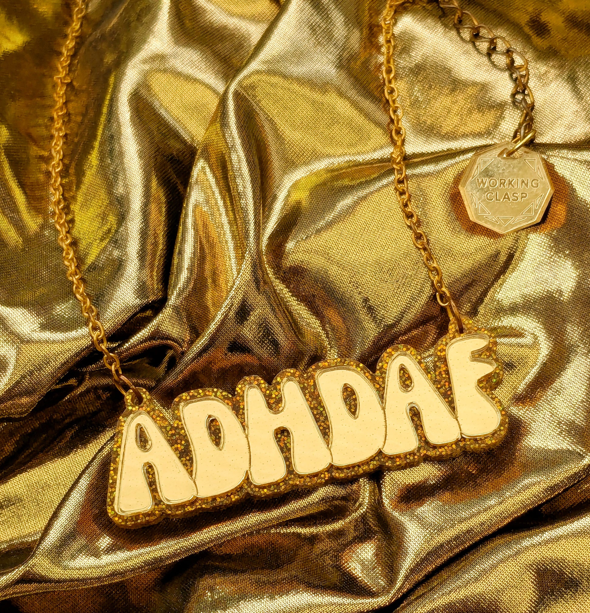 ADHDAF acrylic necklace in gold on a gold chain boxed on a gold fabric background