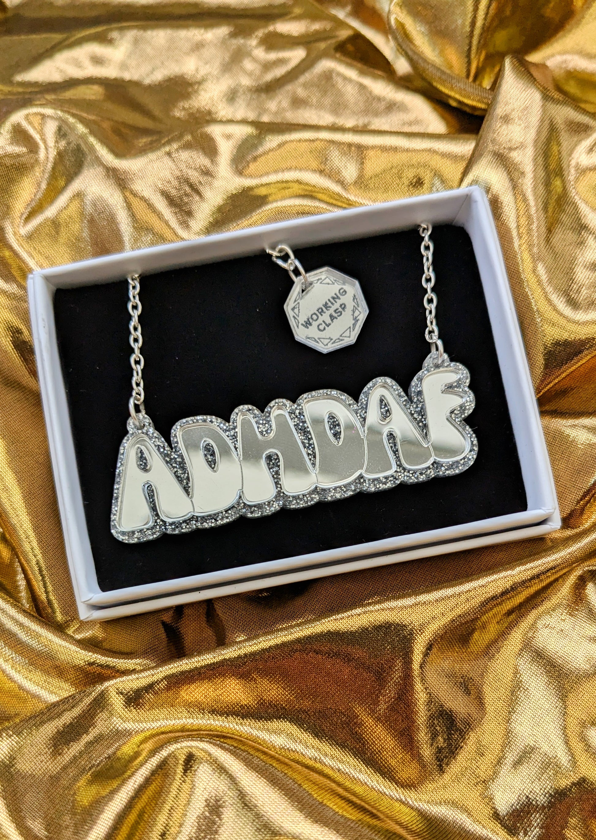 ADHDAF acrylic necklace in silver on silver chain boxed on a gold fabric background