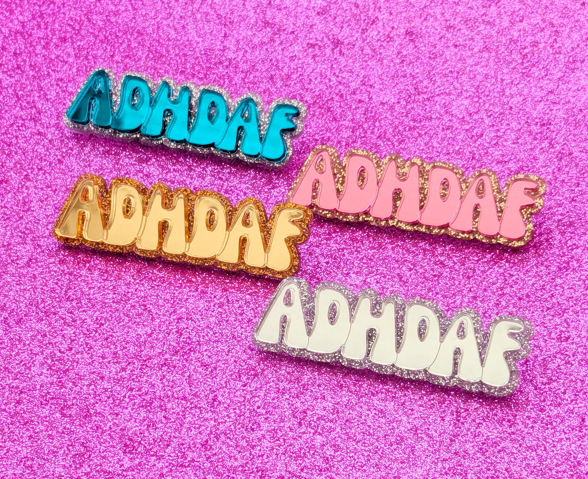 Display of four acrylic brooches in Turquoise, Pink, Gold and Silver each with the writing ADHDAF